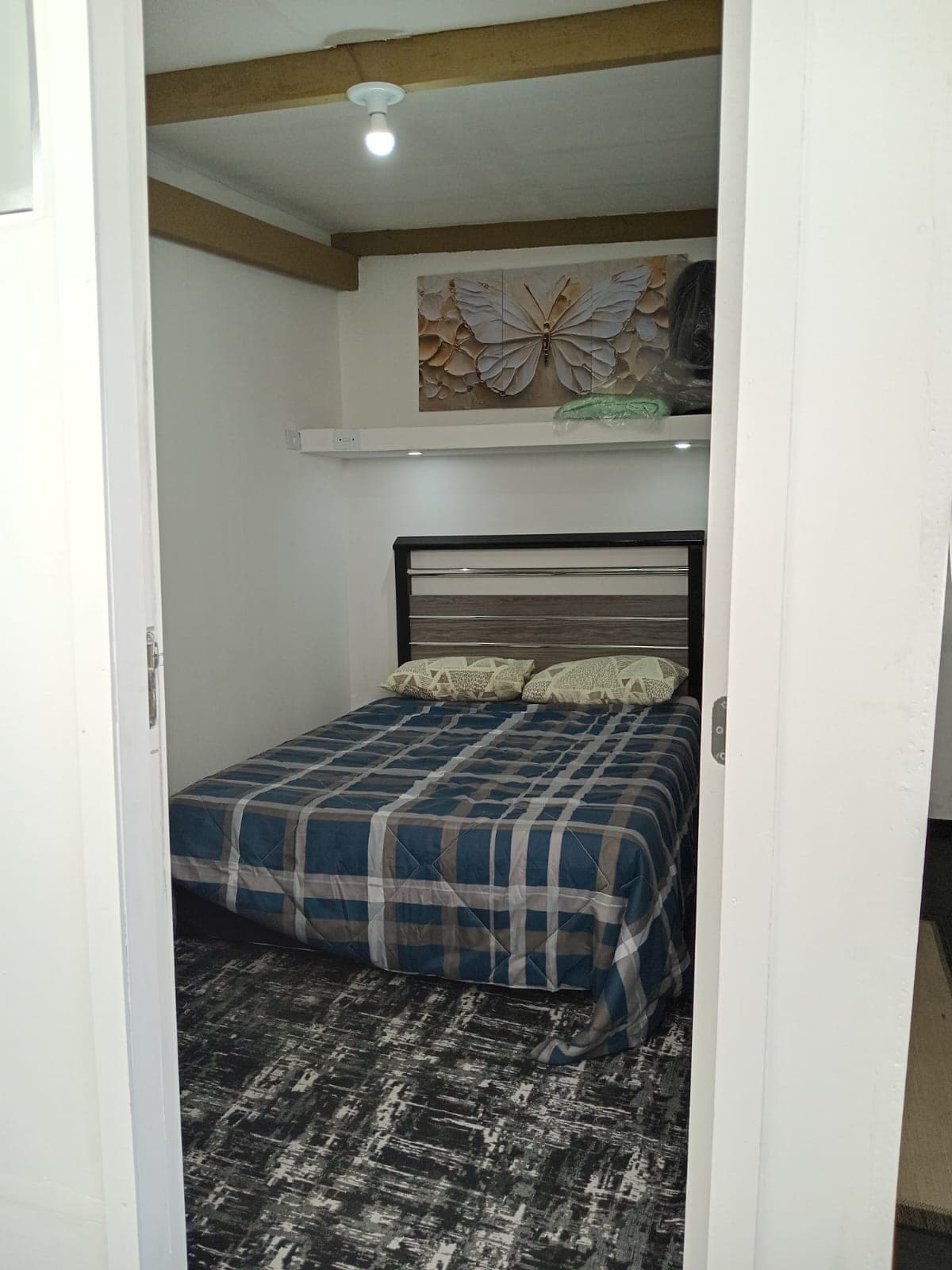 Suíte Borboleta vista da porta, com cama de casal xadrez azul e quadro de borboleta