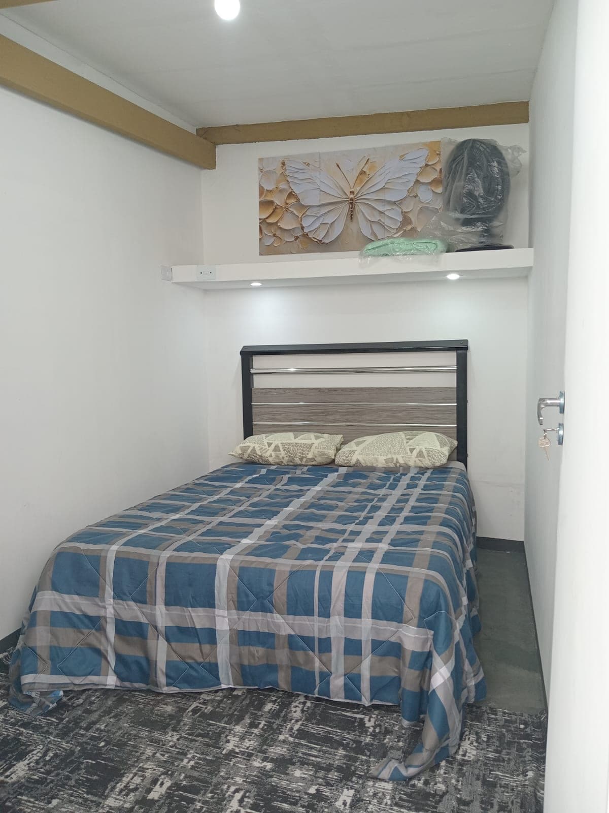 Quarto Borboleta com cama de casal arrumada, quadro de borboleta e ventilador